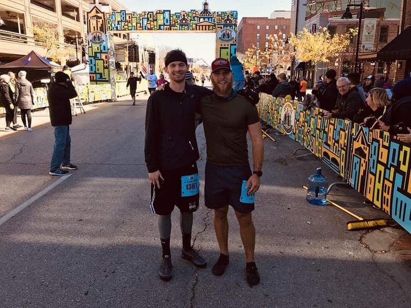 two runners smiling and posing for picture in front of race finish line