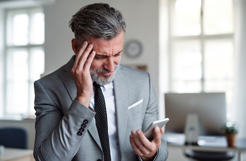 A Frustrated Businessman With Smartphone Standing In An Office, Reading Bad News.