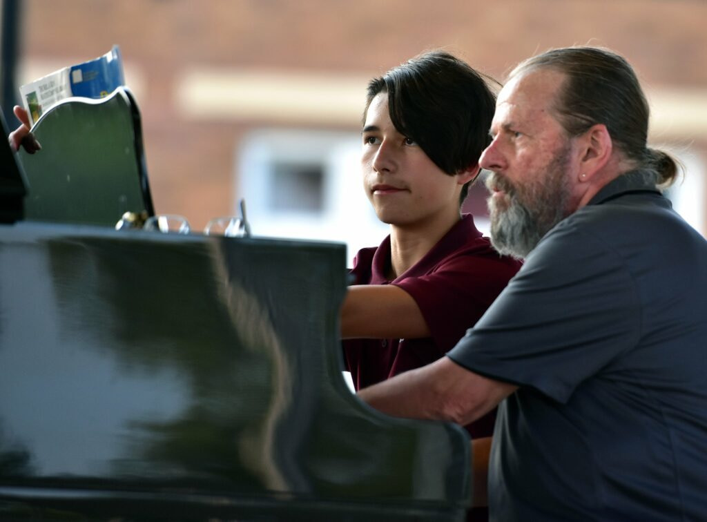 A man sitting next to a younger student at a piano