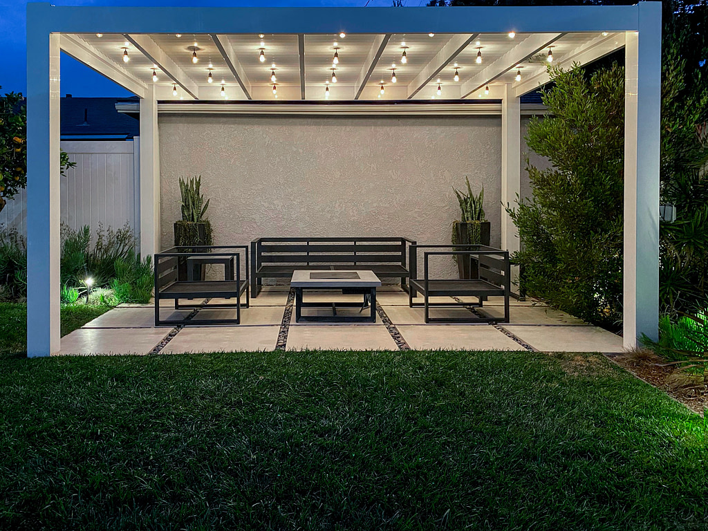 Modern white vinyl pergola over large stone pavers with string lights.
