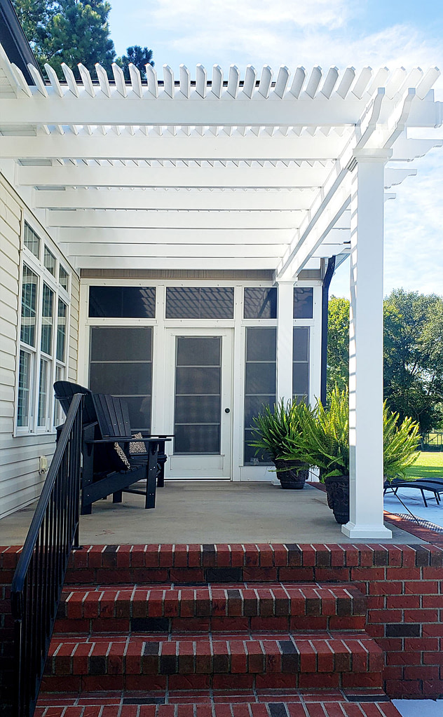 Attached white pergola over a small patio landing on the back of a home