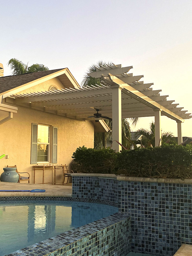 A custom pergola attached to a house with decorative arbor above the beam.