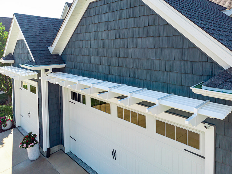 Aerial view of white garage pergola above a double garage door on a blue house.