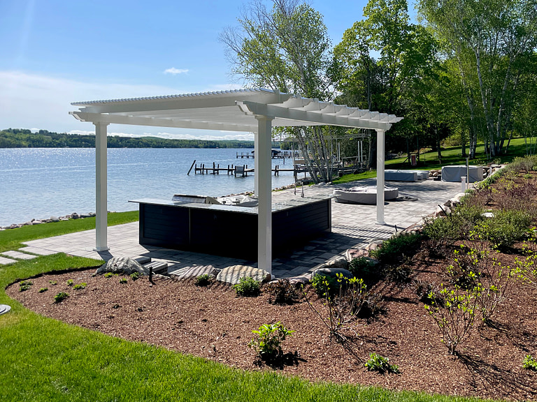 Large freestanding pergola over an outdoor kitchen next to the water.