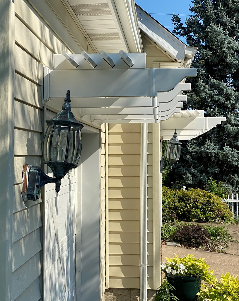 Side profile view of a white vinyl eyebrow pergola on the front of a garage