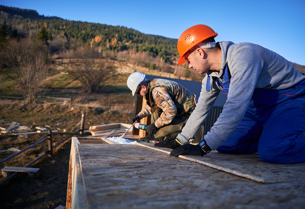 Male Builder Doing Thermal Insulation On Roof Of Wooden Frame House By Polyurethane Foam.