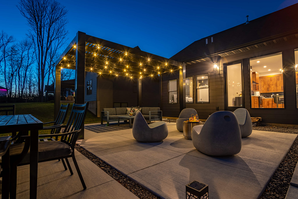 Black modern pergola with string lights at night over patio