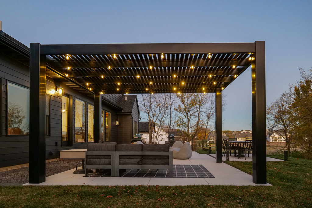 Black modern pergola with string lights at night over patio