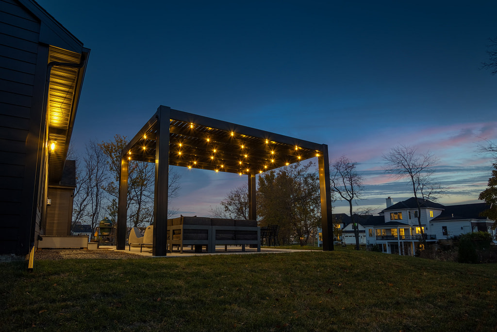 Black modern pergola on a patio at dusk with bistro lights