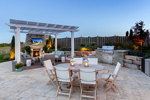 Freestanding white vinyl pergola on a nicely landscaped patio with outdoor fireplace and outdoor seating areas.