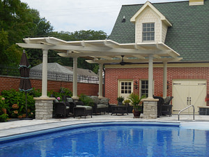 Custom shaped pergola next to a swimming pool on stone columns