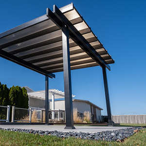 A freestanding patio cover rain proof pergola with bronze polycarbonate roof over patio slab.
