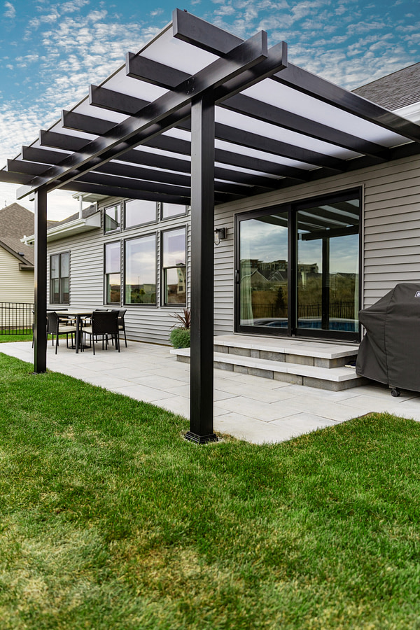 Black rain proof pergola patio cover with white polycarbonate roof over sliding patio doors.
