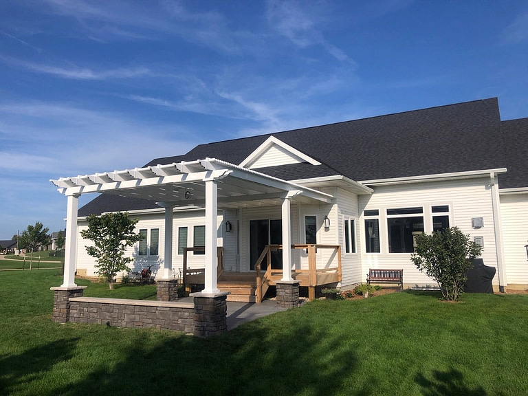 Back of a white house with freestanding white pergola over a patio