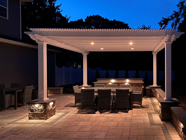 Pergola at night over a paver patio with can lights built into the top of the pergola