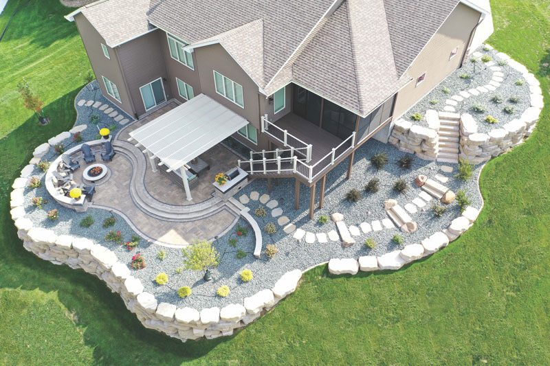 Aerial view of a highly landscaped backyard with stone retaining walls and an attached pergola over a part of the patio.