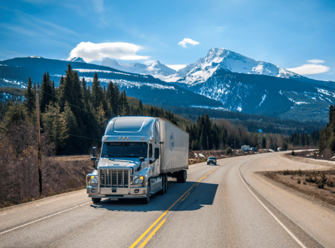Semi-truck driving on highway with mountains in background