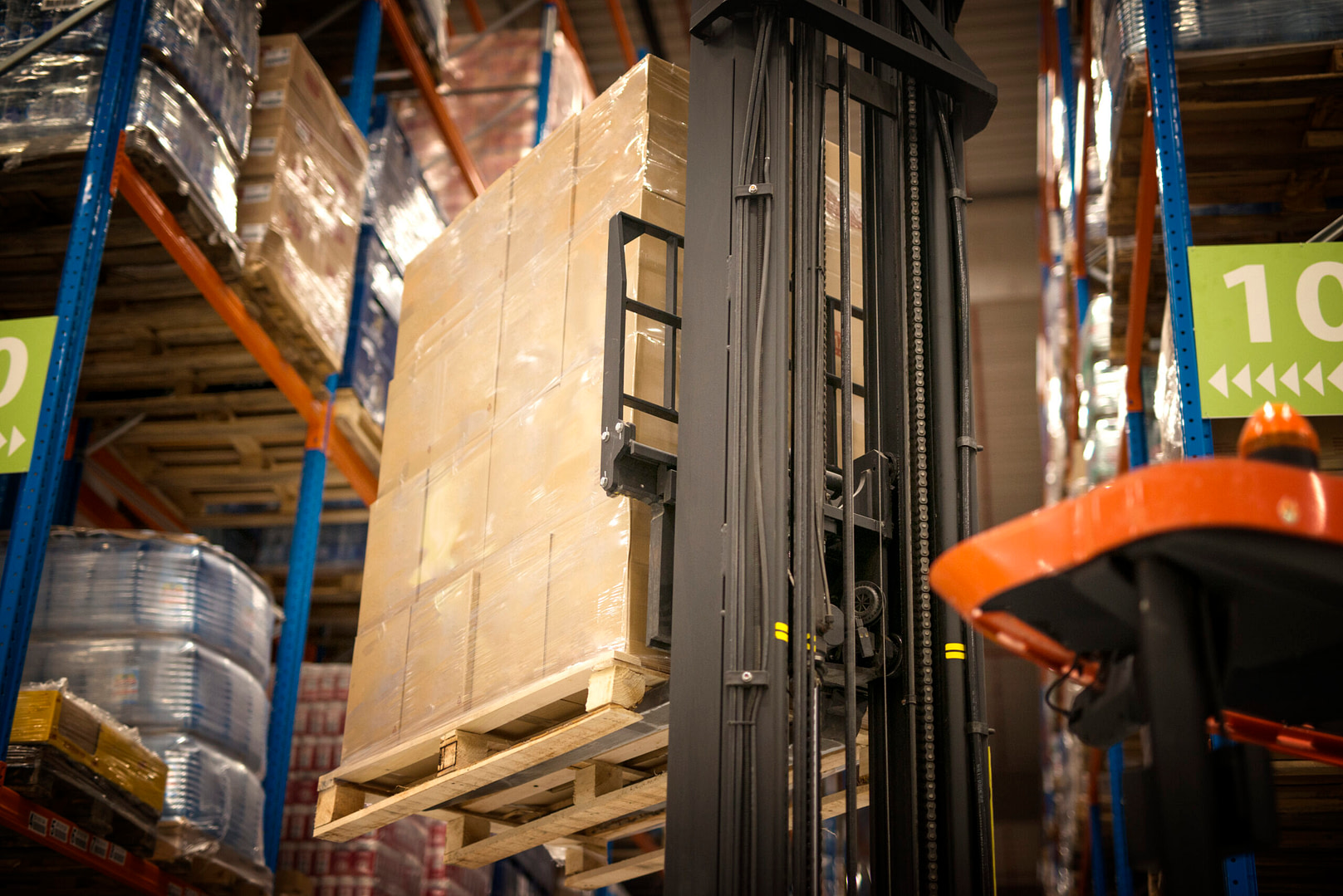 industrial forklift machine lifting palette full of cardboard boxes and placing them on shelves in distribution warehouse facility.