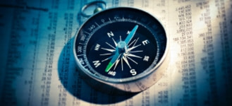 compass laying atop stock section of newspaper