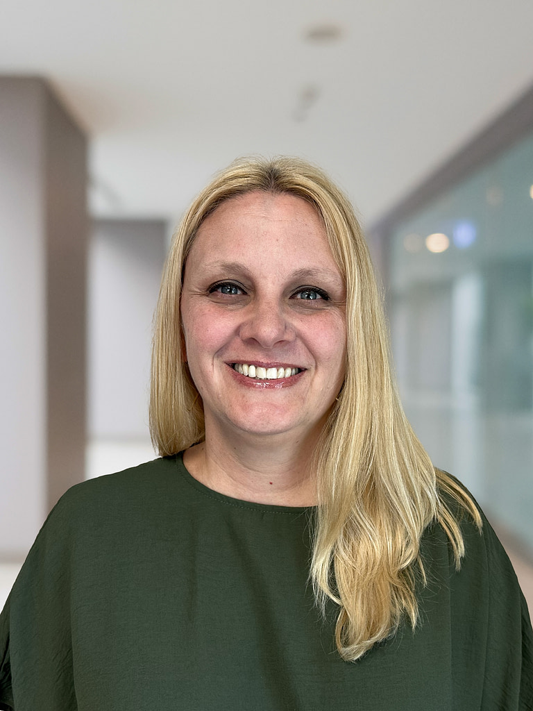 Blonde woman smiling in green top, indoor setting.